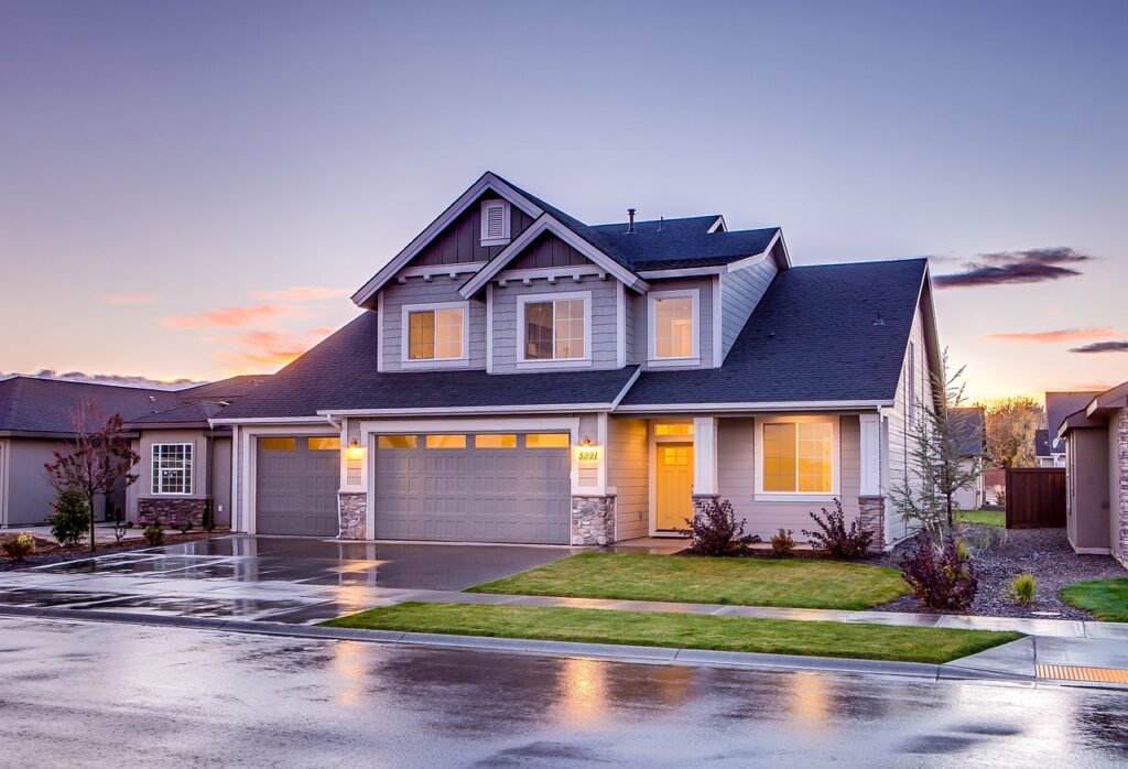 A modern two-story house with a gray exterior, large windows, and a driveway, set against a twilight sky.